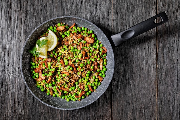 Lebanese warm lentil and green peas salad with bacon lemon zest and lemon and olive oil dressing served on a frying pan on a dark wooden background top view closeup
