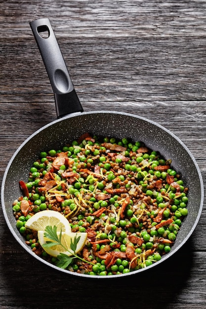 Lebanese warm lentil and green peas salad with bacon lemon zest\
and lemon and olive oil dressing served on a frying pan on a dark\
wooden background top view closeup