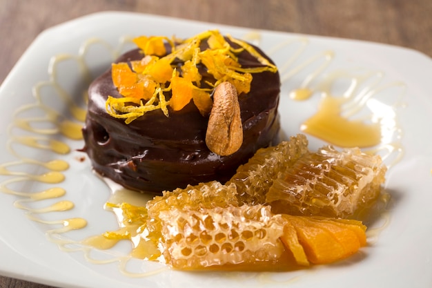 Lebkuchen with pieces of apricot above it in a plate and chocolates and a piece of honeycomb over a wooden surface.