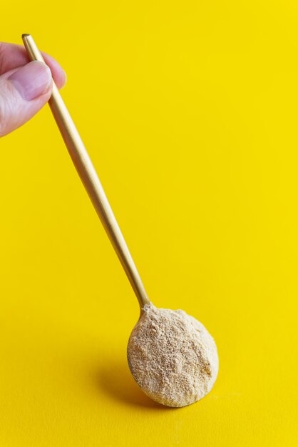 Lecithin powder in a spoon in hand on a yellow