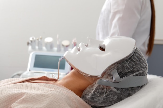 Led-licht anti-aging masker voor gezichtsverzorging in een spa slow motion een vrouw ligt op een bank in een speciaal masker moderne technologieën van schoonheid en gezondheid