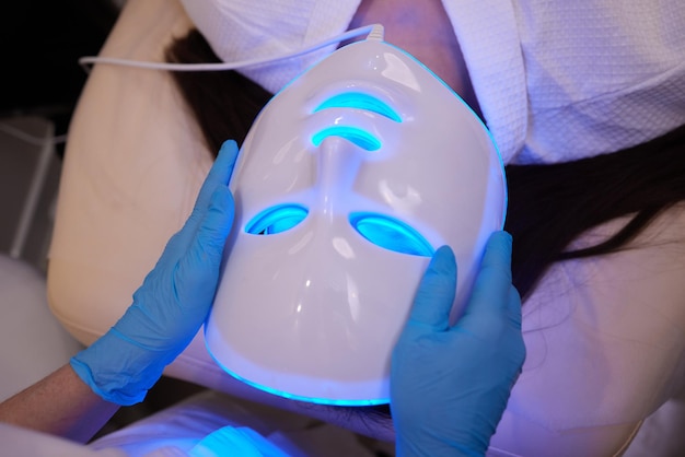 Photo led light antiaging mask for facial skin care in a spa slow motion a woman lies on a couch in a spec...