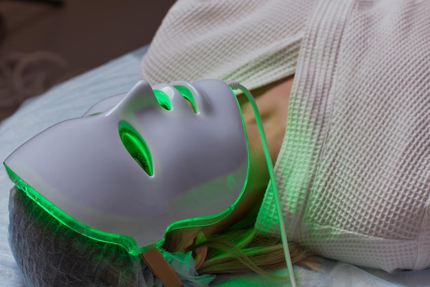 LED light antiaging mask for facial skin care in a spa slow motion A woman lies on a couch in a special mask Modern technologies of beauty and health