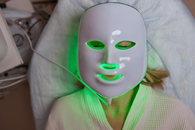 LED light antiaging mask for facial skin care in a spa slow motion A woman lies on a couch in a special mask Modern technologies of beauty and health