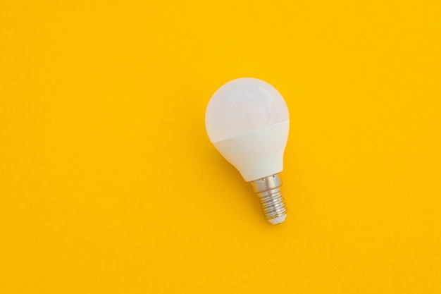 LED light bulb lies on a pastel yellow background Energy saving concept Minimalism top view