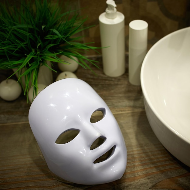 Photo led mask for light therapy on a shelf next to facial skin care products in the bathroom