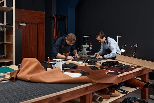 Foto lederen ambachtslieden werken aan het maken van measupenets in patronen aan tafel in de werkplaatsstudio.