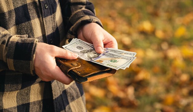 Lederen portemonnee met dollarbiljetten in mannelijke handen op een wazige natuurachtergrond