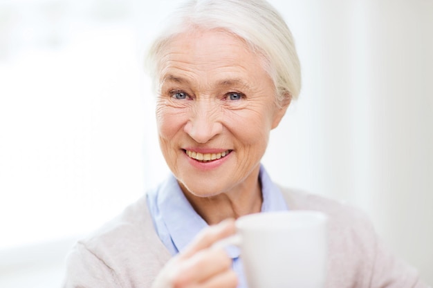 leeftijd, drank en mensenconcept - gelukkige glimlachende hogere vrouw met kop thee of koffie thuis