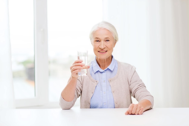 leeftijd, gezondheidszorg en mensenconcept - gelukkige hogere vrouw met glas water thuis