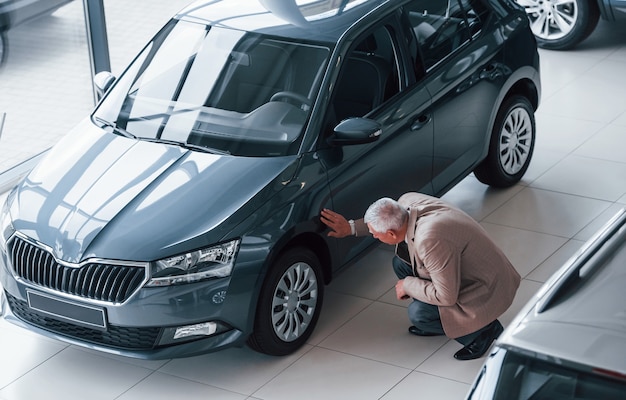 Leeftijd man in formele kleding wandelen in de auto salon en op zoek naar de auto.