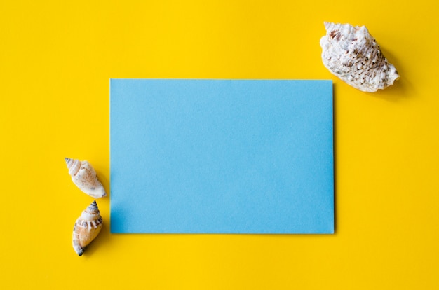 Leeg blauw vel papier op gele achtergrond met schelpen. Zomer achtergrond.