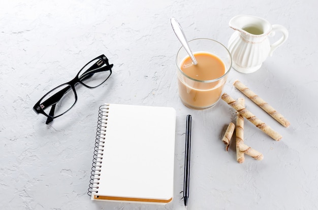 Leeg dagboek, pen, kopje koffie en een bril op grijze achtergrond