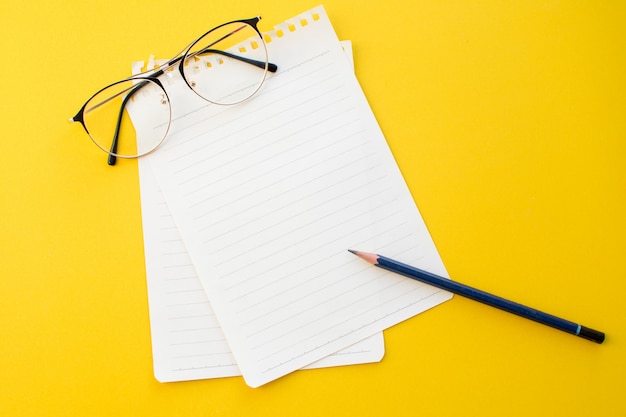Leeg document van notitieboekjeglazen en potlood op gele achtergrond met schoolconcept.