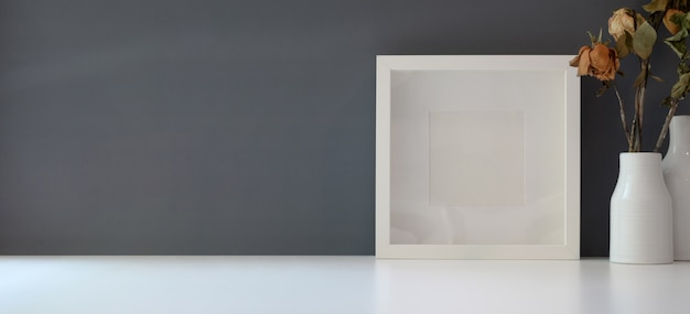 leeg frame met droge rozenvaas in moderne werkruimte op witte tafel en donkergrijze muur