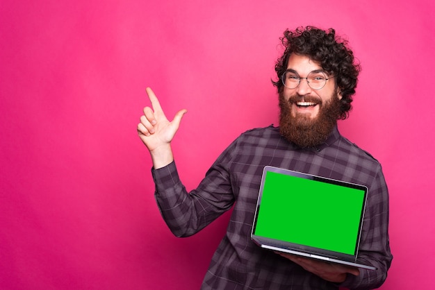 Leeg groen scherm op laptop, gelukkig man met baard glimlachend en weg wijzen en laptop vast te houden