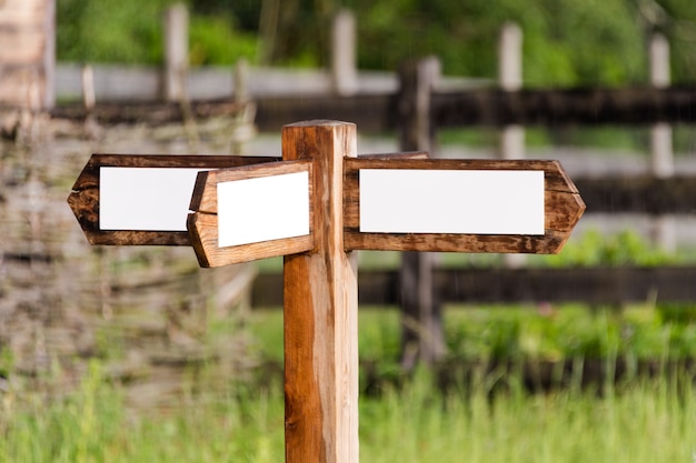 Foto leeg houten bord met pijlen op de ranch. eenvoudig houten bord met drievoudige richtingspijl in de tuin met houten omheining