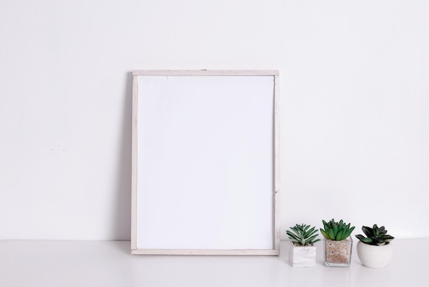 Leeg houten verticaal frame en groene kamerplanten bloemen op tafel tegen witte muur achtergrond. Mo