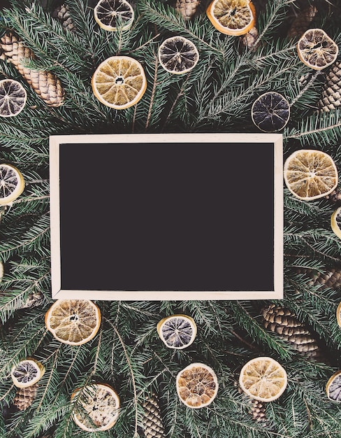 Leeg ingelijst bord op groene dennentakken versierd met gedroogde sinaasappelschijfjes en kegels. Nieuwjaar vintage wintervakantie feestelijke compositie.