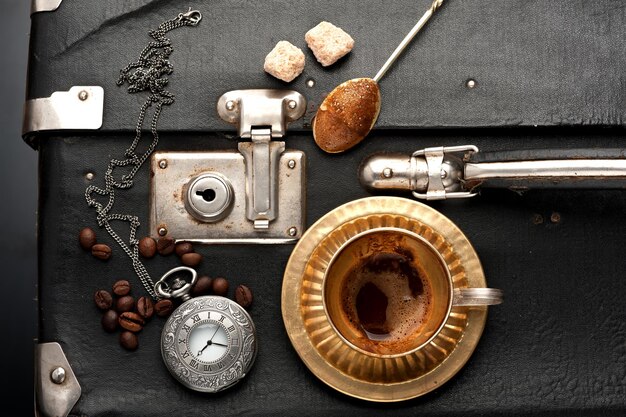 Leeg koffiekopje horloge aan een ketting en vintage koffer in retrostijl