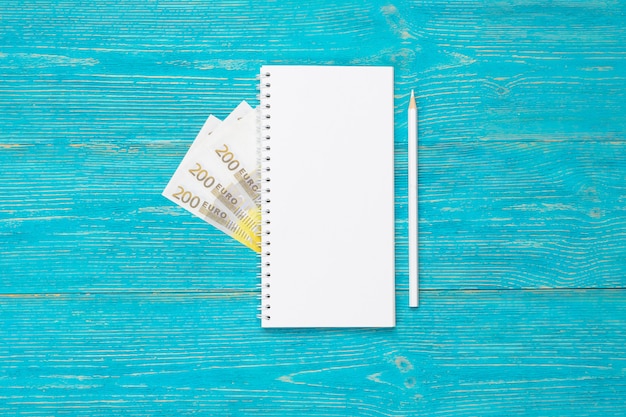 Leeg notitieblok met wit potlood en 200 euro-bankbiljetten op turquoise houten tafel, kopie ruimte