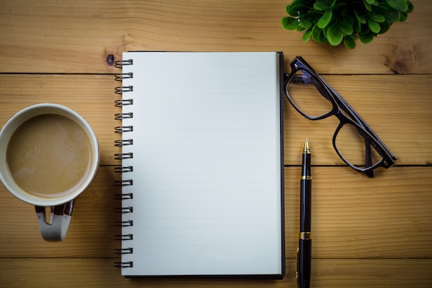 Leeg notitieboekje met pen en met glazen naast kop van koffie op houten lijst