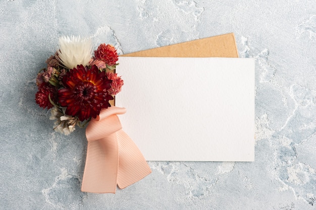 Leeg papier en kraft envelop met rood boeket droge bloemen. Bruiloft mock up op grijze tafel