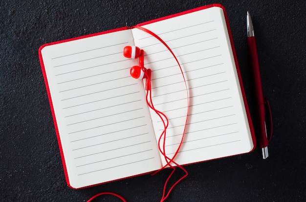 Leeg rood notitieboekje met rode pen en oortelefoons