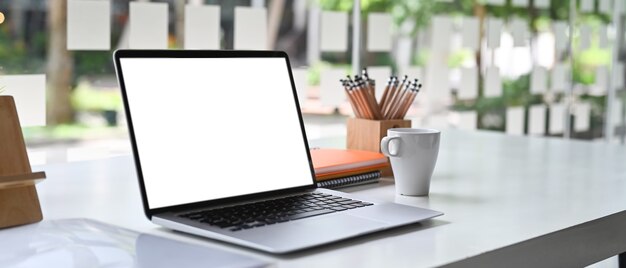 Leeg scherm laptopcomputer en een kopje koffie op wit bureau