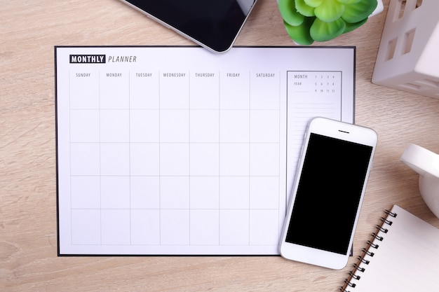 leeg scherm smartphoneplanner schema en kantoorbenodigdheden op houten achtergrond