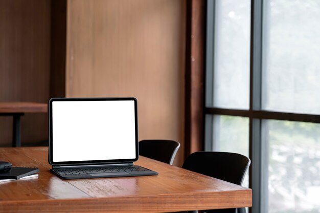 Leeg scherm tablet met magisch toetsenbord en gadget op houten tafel in vergaderruimte.