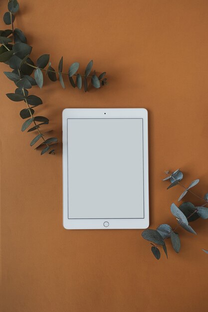 Leeg scherm tablet pad met eucalyptustak op diep oranje