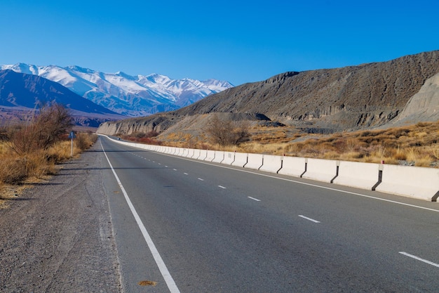 Leeg snelwegweg met scheidende betonnen barrière in de bergen op een zonnige herfstdag