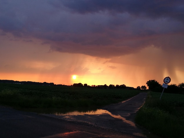 Leeg weg bij veld tegen bewolkte lucht bij zonsondergang