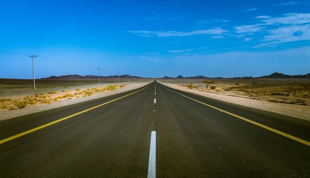 Leeg weg langs het landschap tegen de blauwe hemel