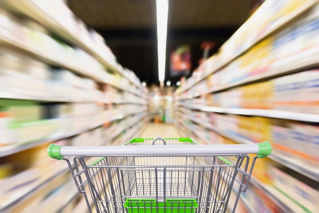 Leeg winkelwagentje met vervagen supermarkt gangpad met baby formule melkproduct op de plank, bewegingsonscherpte