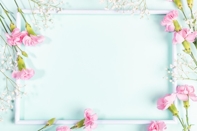 Leeg wit frame met zachte roze anjers en witte gypsophila bloemen erop op pastel lichtblauwe achtergrond Happy Mothers of Valentijnsdag Uitzicht van bovenaf Kopieer ruimte Vakantie mock up