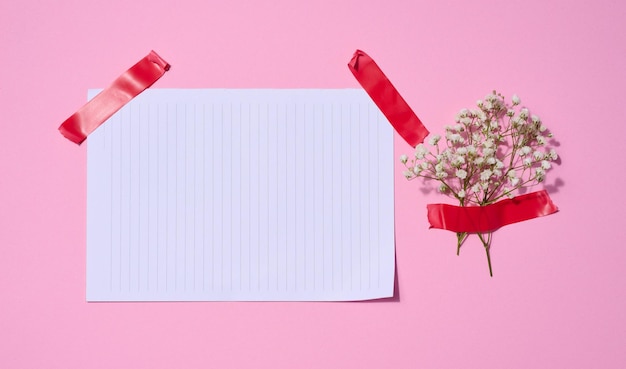 Leeg wit vel papier en gypsophilia bloemen op een roze achtergrond ruimte voor een inscriptie