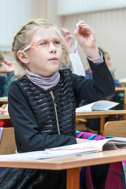 Foto leerling met bril zit aan een schoolbank en schrijft met een pen in de lucht