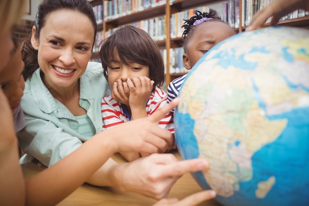 Leerlingen en leraar kijken naar globe in de bibliotheek