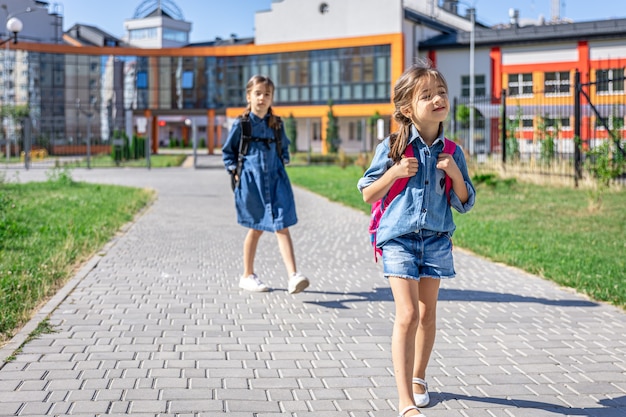 Leerlingen van de basisschool. Meisjes met rugzakken in de buurt van buiten bouwen. Begin van de lessen. Eerste dag van de herfst.