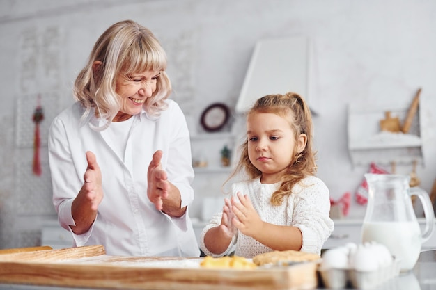 Leerproces senior grootmoeder met haar kleine kleindochter kookt snoep voor kerstmis in de keuken