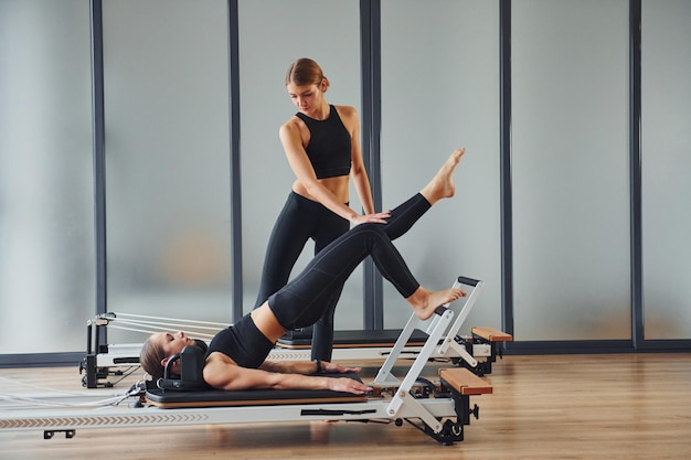 Leert nieuwe oefeningen Twee vrouwen in sportieve kleding en met slanke lichamen hebben samen fitness-yogadag binnenshuis