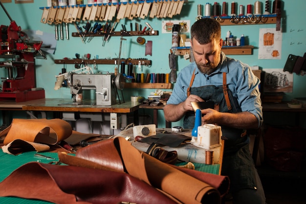 Leervakman die met natuurlijk leer met behulp van hamer werkt. Handtasmeester aan het werk in lokale workshop.