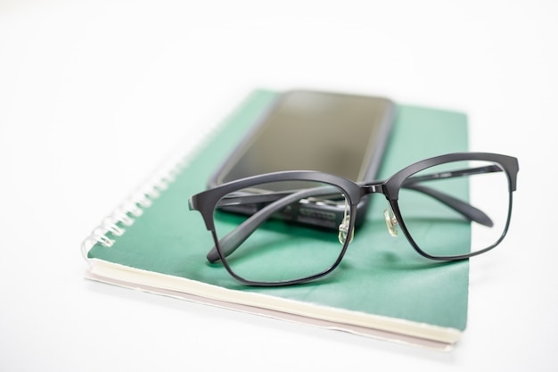 leesbril op mobiele smartphone en groene laptop op witte tafel.