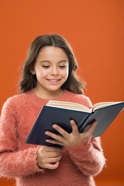 Leesoefening voor kinderen. Meisje houdt boek gelezen verhaal over oranje achtergrond. Kind geniet van het lezen van boek. Boekwinkelconcept. Prachtige gratis kinderboeken beschikbaar om te lezen. Kinderboeken.