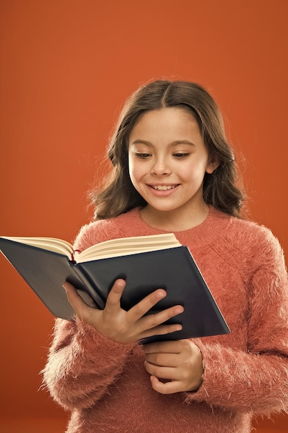 Leesoefening voor kinderen Meisje houdt boek lees verhaal over oranje achtergrond Kind geniet van het lezen van boek Boekwinkelconcept Prachtige gratis kinderboeken beschikbaar om kinderliteratuur te lezen