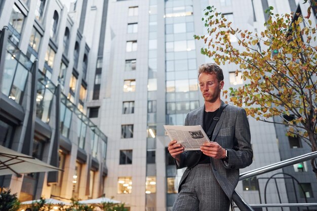 Leest krant Jonge elegante man in goede kleren is overdag buiten in de stad