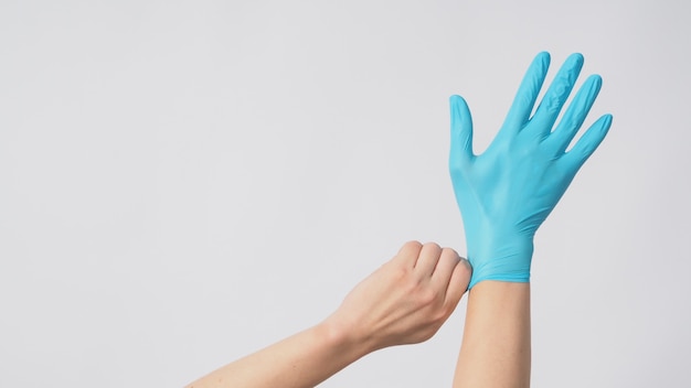 Left hand is pulling right hand with blue latex gloves on white background.