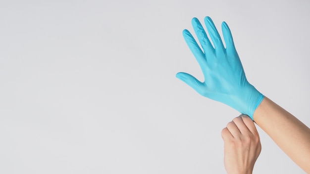 Left hand is pulling right hand with blue latex gloves on white background.